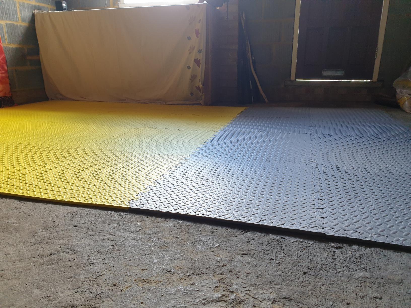Yellow and grey interlocking gym flooring mats / 60×60 interlocking floor tiles covering a rough garage floor as a home workout area
