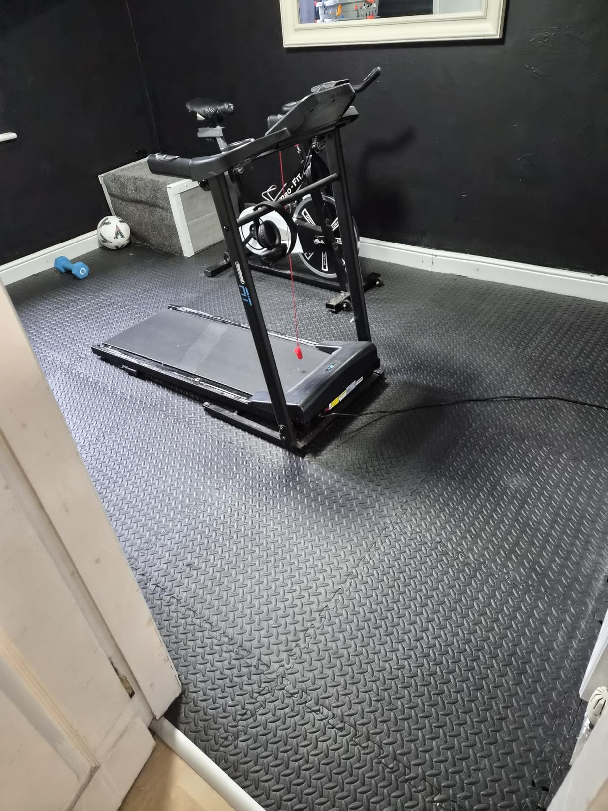 Grey interlocking gym flooring mats under a treadmill and exercise bike in a home gym
