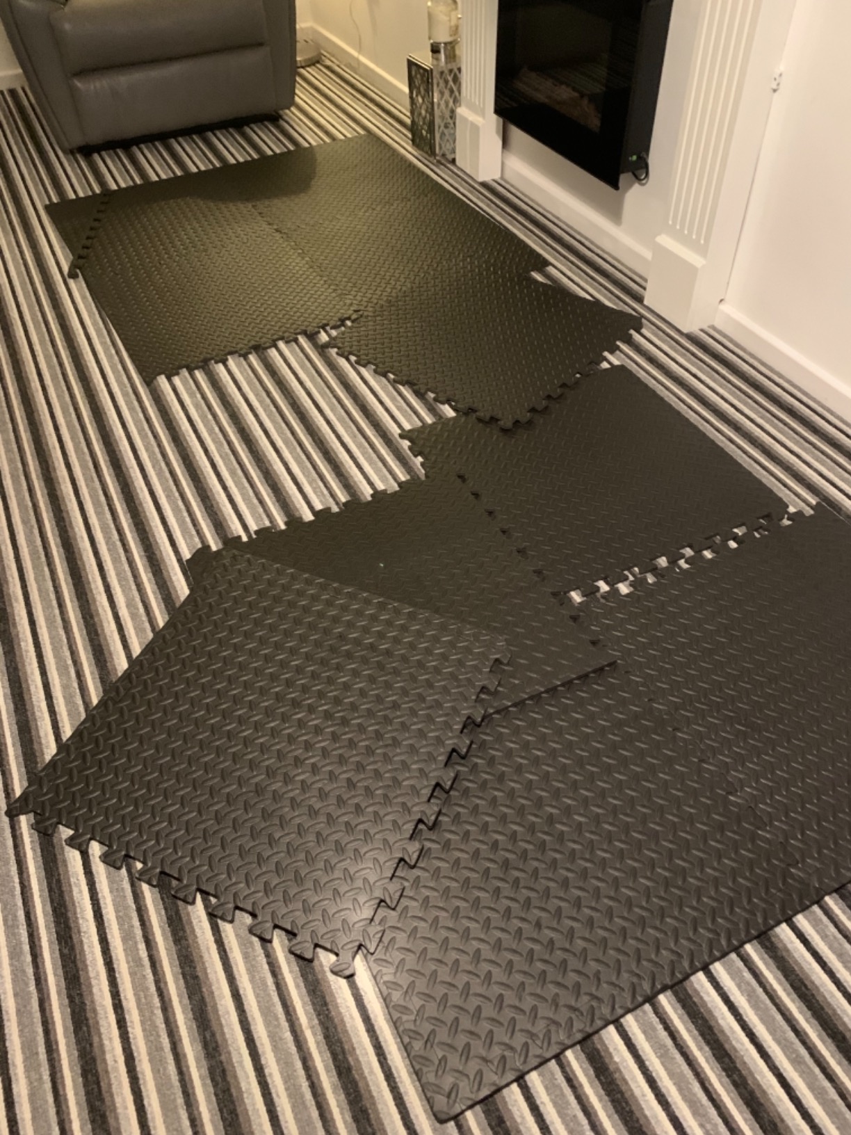 Black checker-plate interlocking floor tiles laid out in a living room beside a fireplace