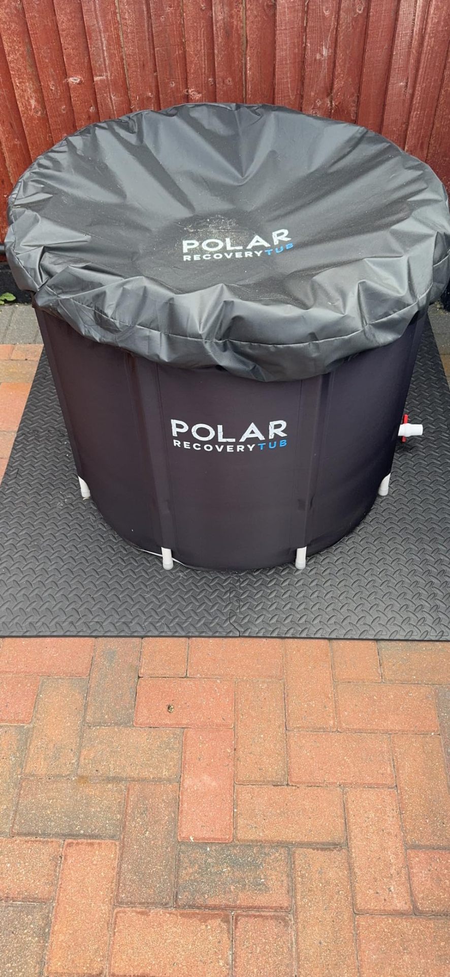 Black extra-thick 2cm reversible interlocking gym mats used as a protective base under a Polar recovery ice tub on a patio