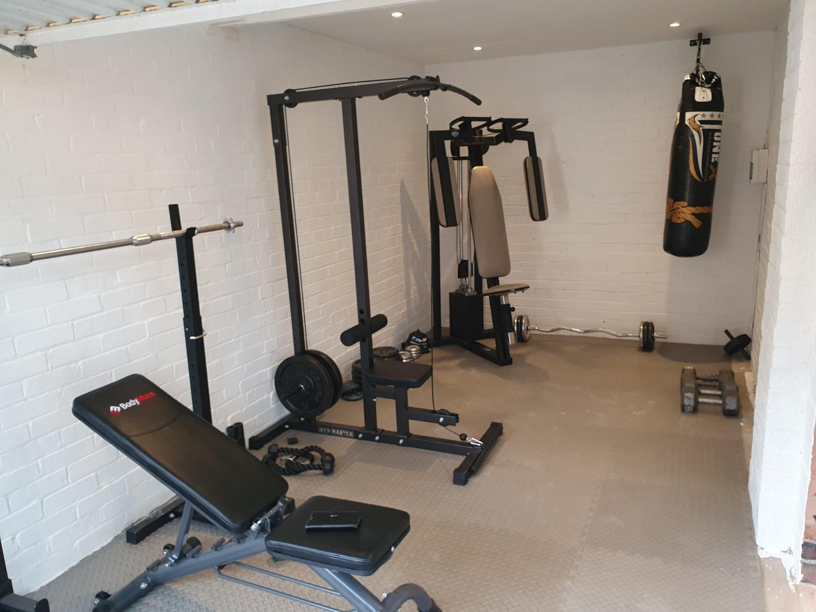 Beige 60×60 interlocking EVA gym flooring tiles covering a garage home gym with a multi-gym, weights bench and punch bag