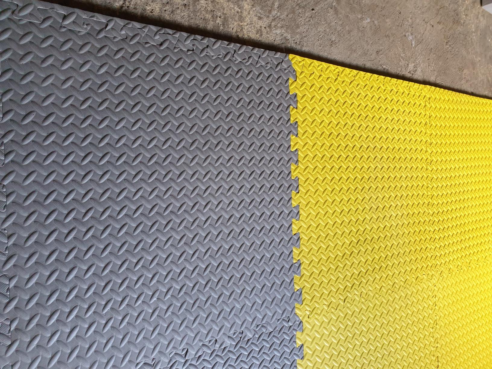 Close-up of yellow and grey 60×60 interlocking EVA floor tiles showing the checker-plate texture and jigsaw edges locking together