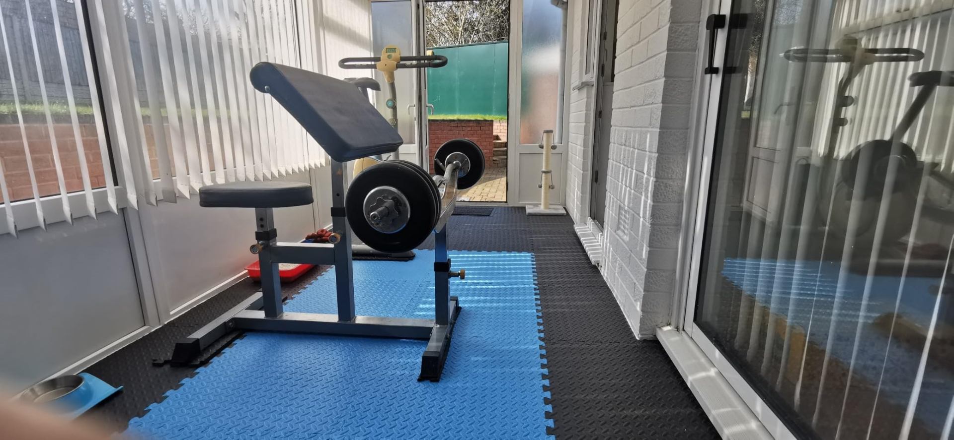 Blue and black 60×60 interlocking EVA gym flooring tiles covering a conservatory home gym with a weights bench