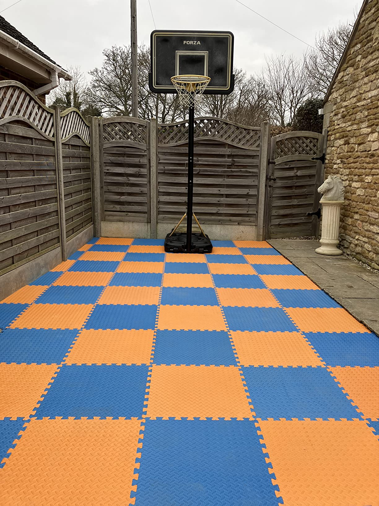 Orange and blue 60×60 interlocking EVA floor tiles laid over patio slabs to make an outdoor basketball court